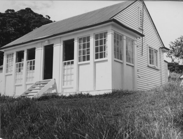 A black and white photo of a house with grilled windows and stairs leading down to a grassy verge.